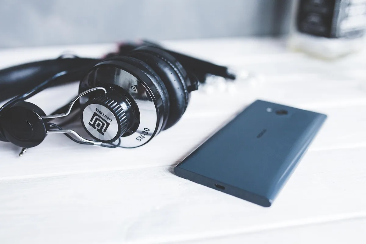 Hand holding a smartphone and vintage headphones with vinyl records in the background