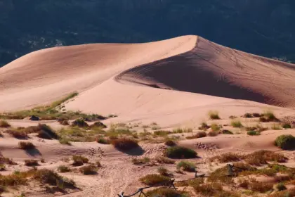 Hands adjusting cloth wrappings and a satchel on sunlit desert dunes under blue sky