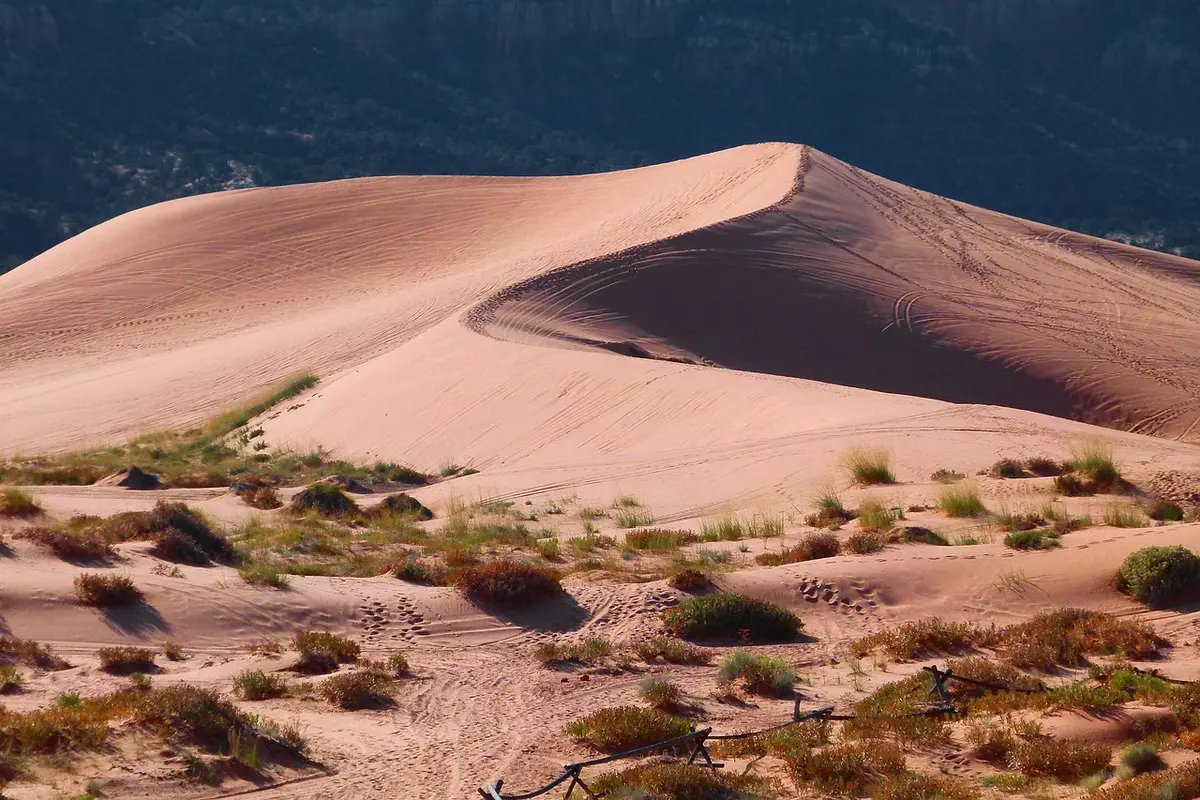 Hands adjusting cloth wrappings and a satchel on sunlit desert dunes under blue sky