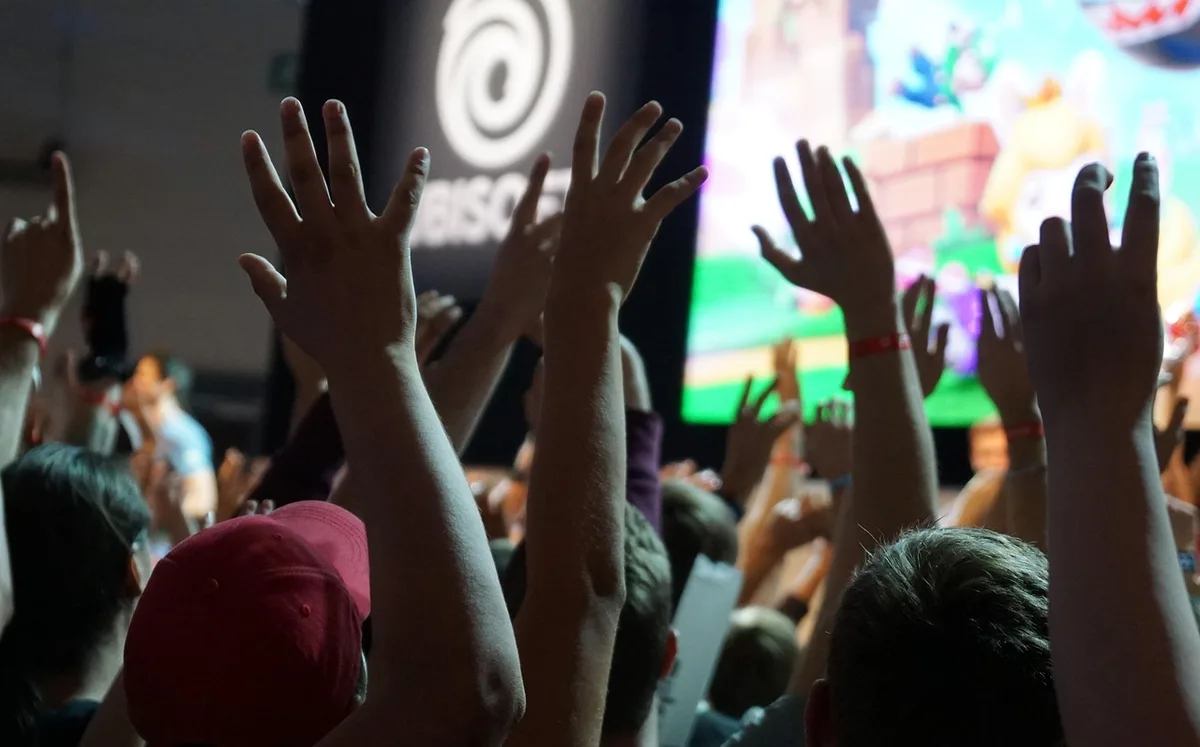 Visitors at a gaming convention floor with hands-on demo stations and queues