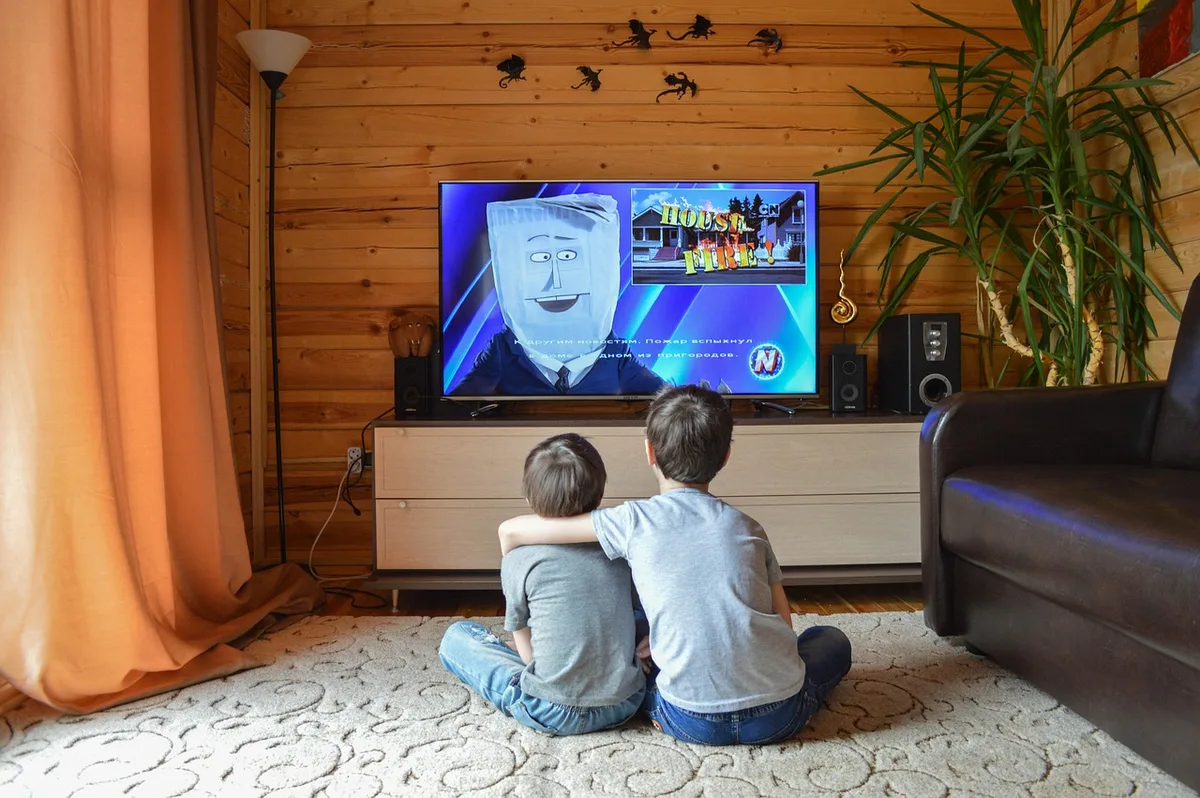 TV screen showing streaming app menus beside Blu-ray cases on a shelf
