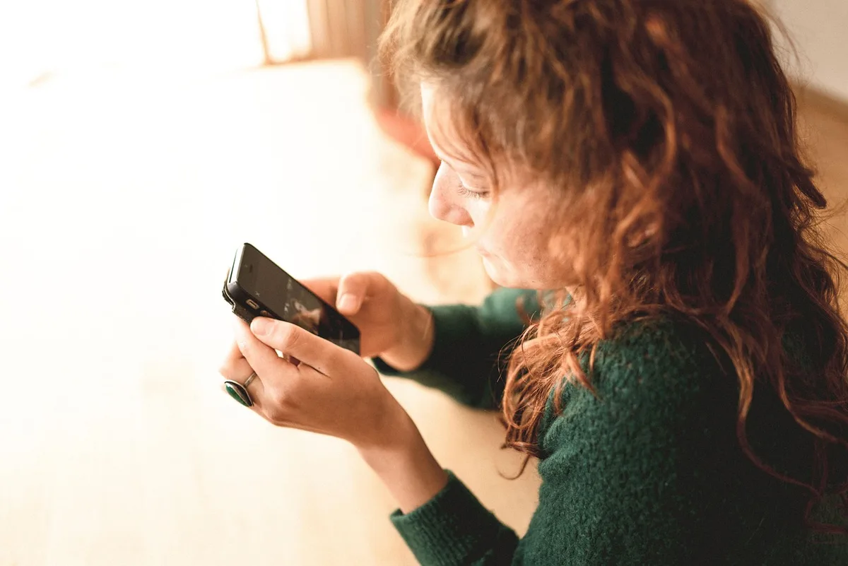 Hand holding phone showing a public social post of a chair, with a gaming chair blurred in background